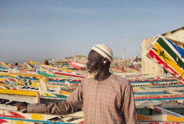 Man framför färgglada båtar på strand i Senegal.