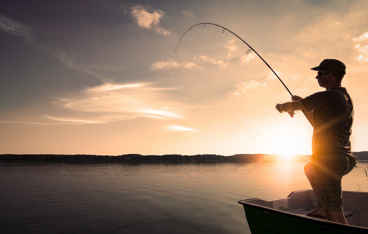 Man fiskar från båt i solnedgång.