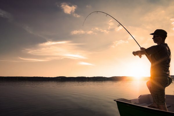 Man fiskar från båt i solnedgång.