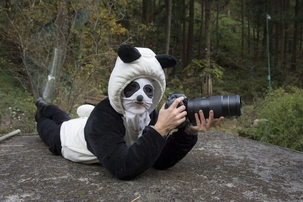 Ami Vitale ligger iklädd en svartvit dräkt som ser ut som en panda. Hon ligger på en klippa och fotograferar med ett långt teleobjektiv.