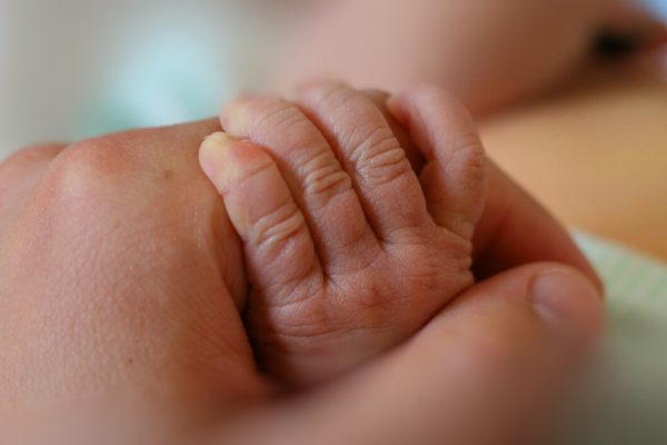 Liten bebishand håller tag runt pekfingret på en vuxens hand