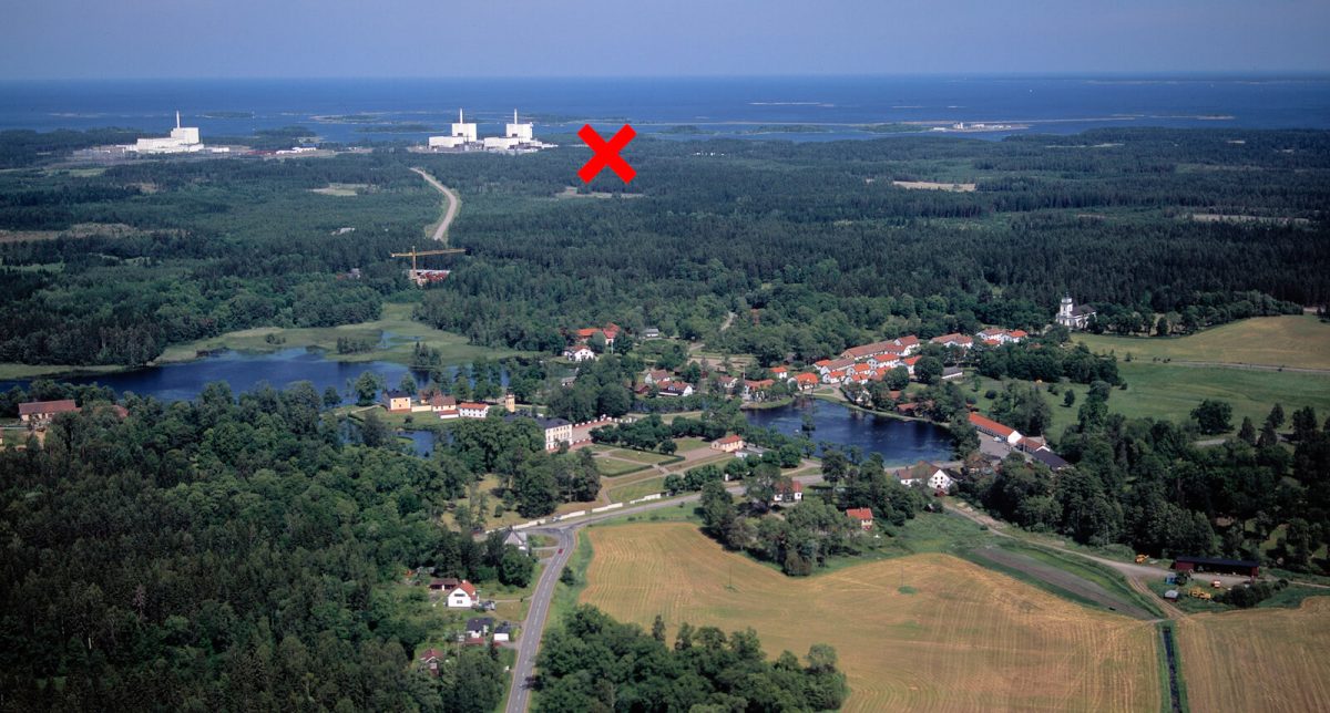 Kryss på flygbild över Östhammar där man ser åkrar, skog, röda hus och i bakgrunden kärnkraftverk.