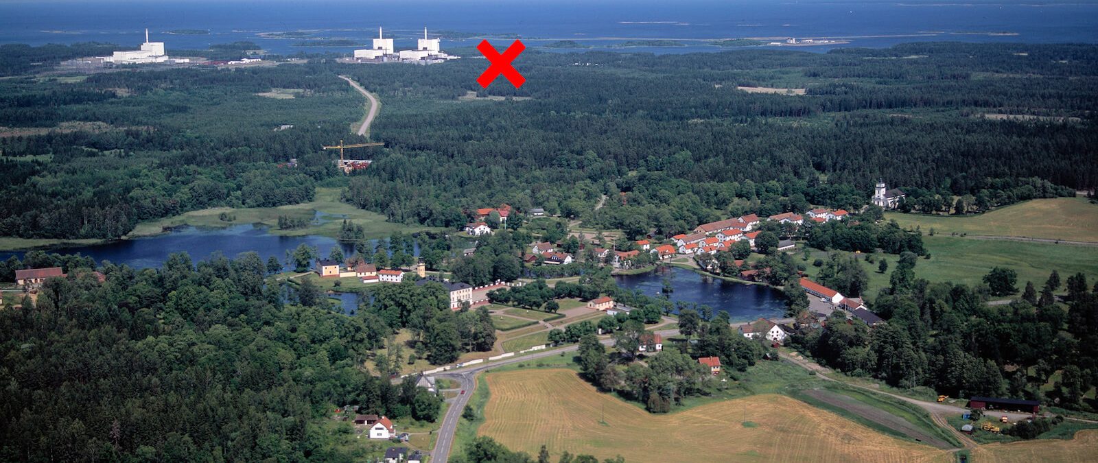 Kryss på flygbild över Östhammar där man ser åkrar, skog, röda hus och i bakgrunden kärnkraftverk.