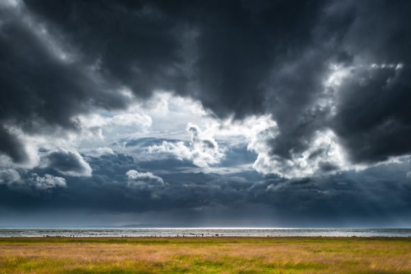 Mörka moln över hav och ängsstrand.