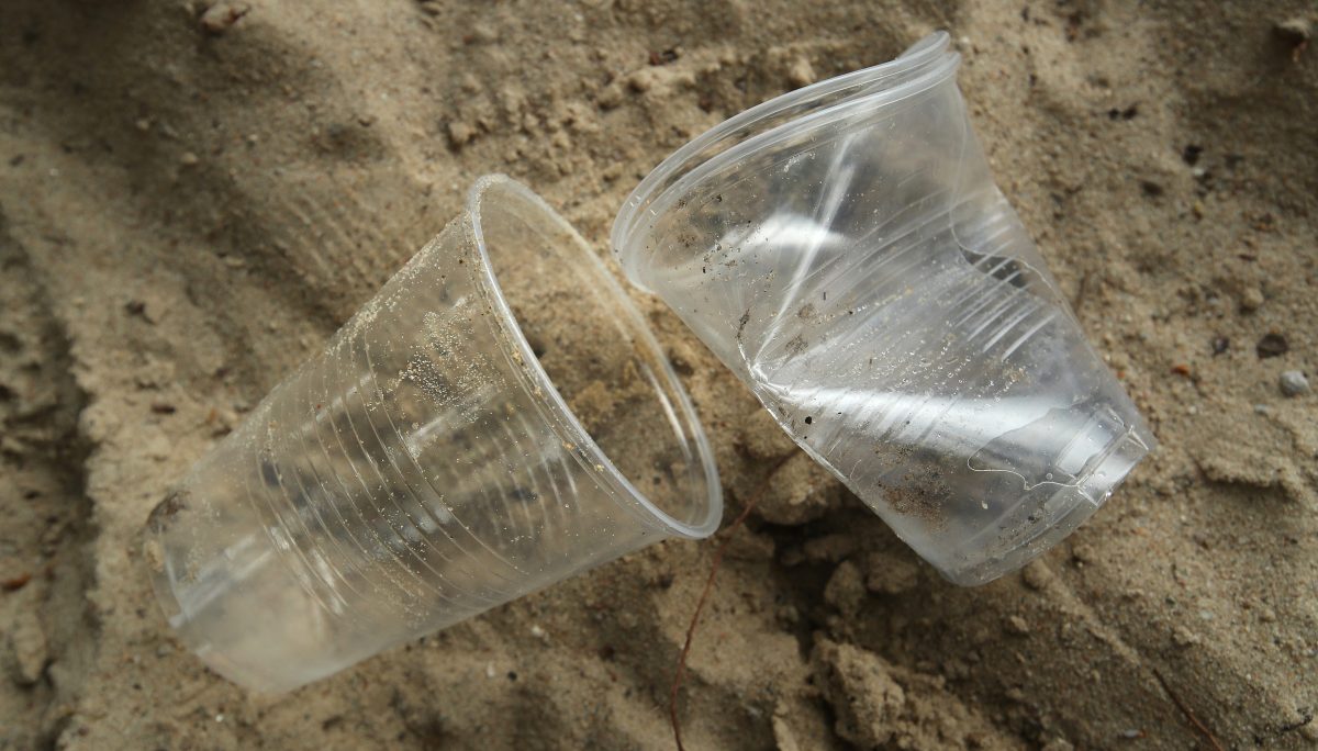 Förbrukade engångsglas i plast ligger slängda på en sandstrand.