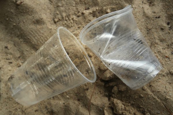 Förbrukade engångsglas i plast ligger slängda på en sandstrand.