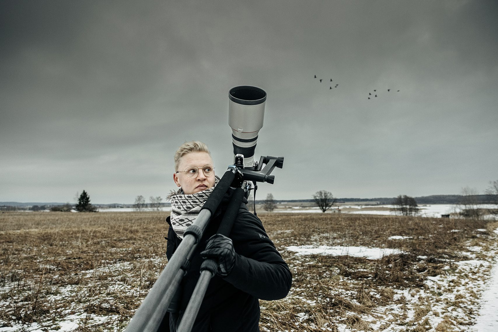 Fotografen Jonas Classon med stativ och kamera med långt teleobjektiv. I bakgrunden sjön Tysslingen och en flock fåglar.