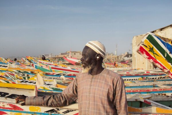 Man framför färgglada båtar på strand i Senegal.