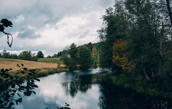 Lugnt vatten i å med åkerlandskap.
