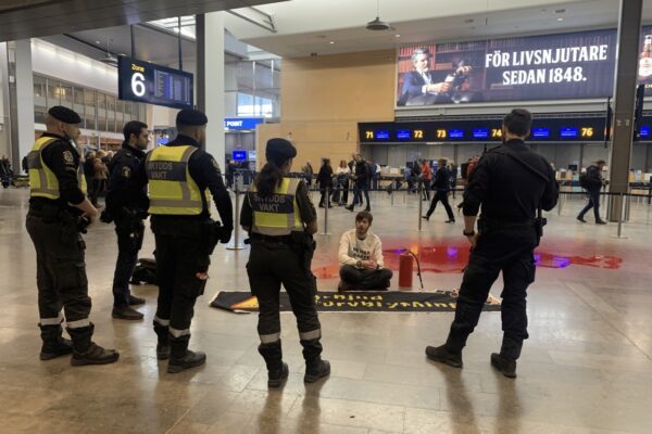Klimataktivist på golv med röd färg, framför polis och ordningsvakter.