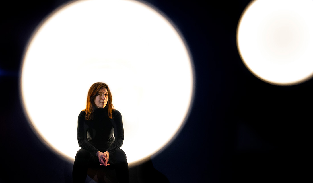 Lisa Röstlund sitter i ett mörkt rum med en lysande cirkel bakom sig.