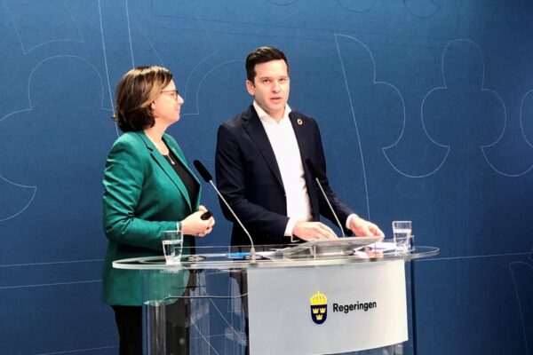 Kvinna i dräkt och man i kostym vid podium.