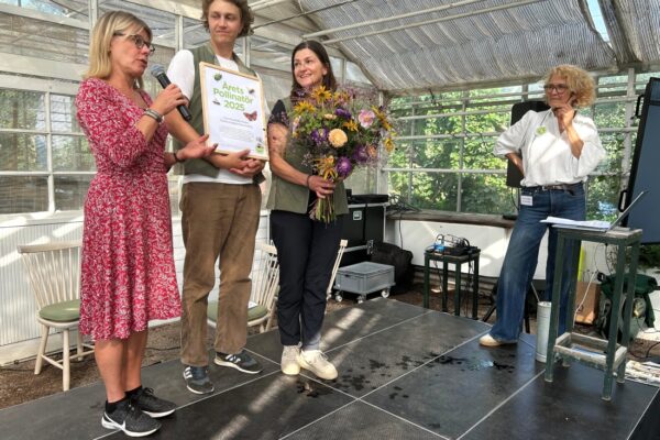Prismottagare på scen med blommor och diplom.